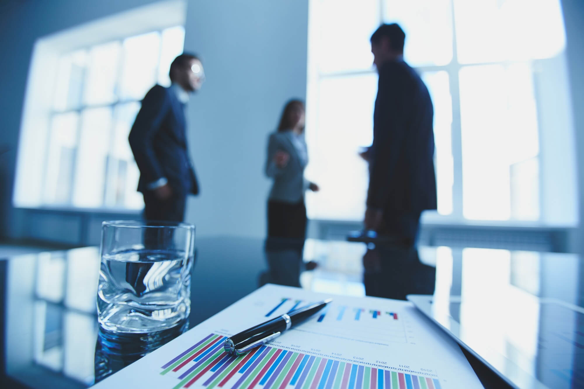 Business meeting with charts, pen, water glass, and blurred figures.